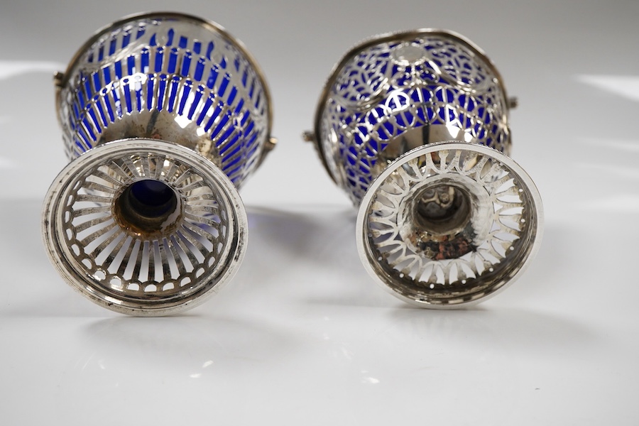Two George III pierced silver pedestal sugar baskets, with blue glass liners, spiral handle, Burridge Davenport, London, 1777, the other William Plummer, London, 1775, tallest 10.1cm excluding the handle.